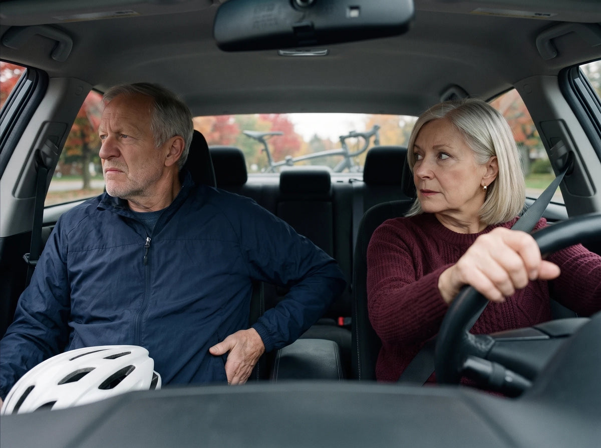 Dans l'auto, Lucie au volant le regarde ; lui, côté passager, le casque sur les genoux, regarde dehors, la main appuyée sur le siège sous sa hanche ; le vélo sur le support, en arrière