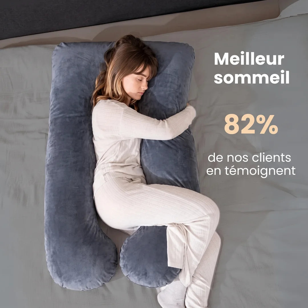 Une femme dort sur le côté, blottie contre un grand coussin en U en velours gris : « Meilleur sommeil — 82 % de nos clients en témoignent »