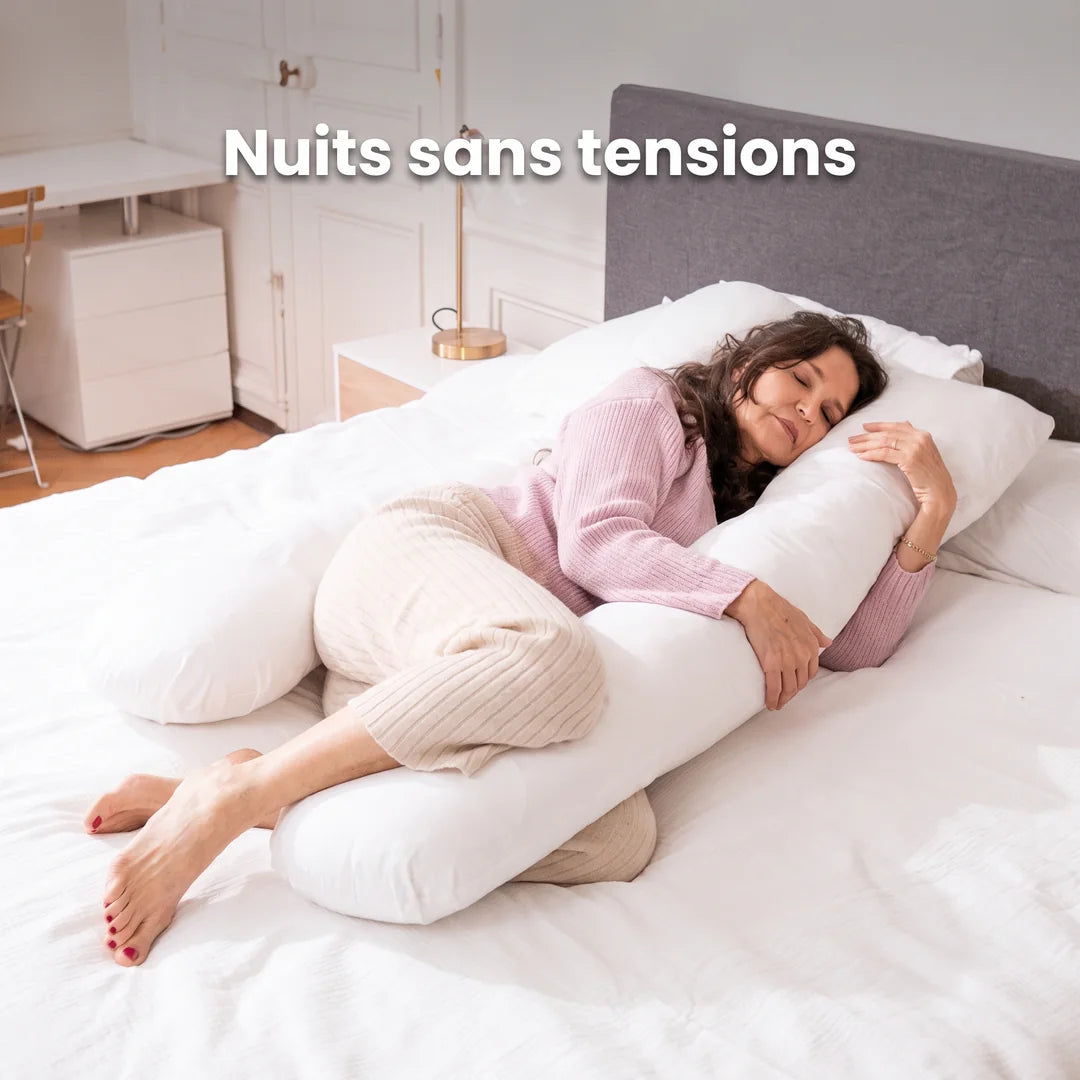 Une femme dort sur le côté, le dos et les genoux soutenus par un grand coussin en U blanc : « Nuits sans tensions »