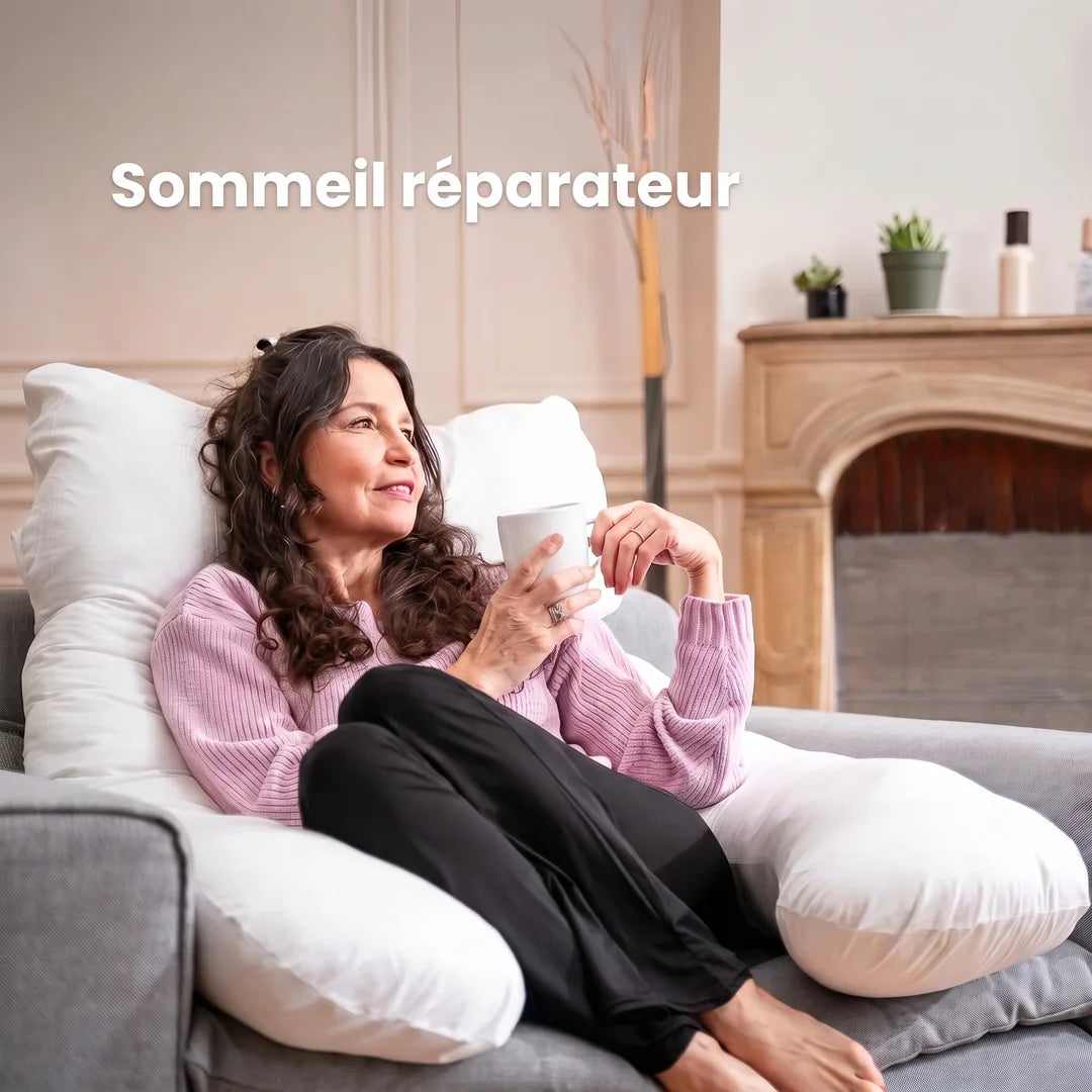 Une femme détendue sur le divan, une tasse à la main, adossée à un grand coussin en U blanc : « Sommeil réparateur »