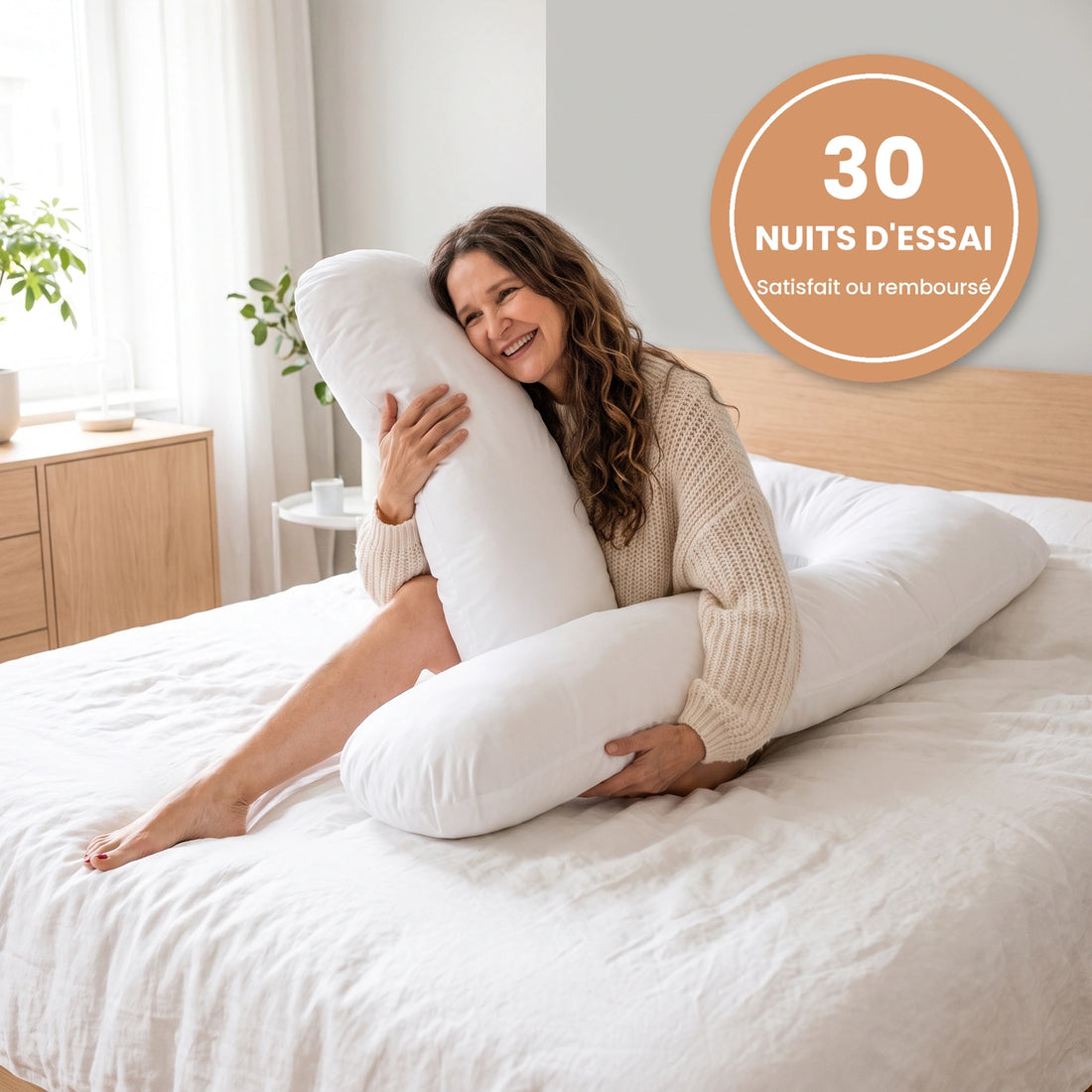 Une femme souriante serre son coussin en U blanc sur son lit, avec le sceau « 30 nuits d'essai »