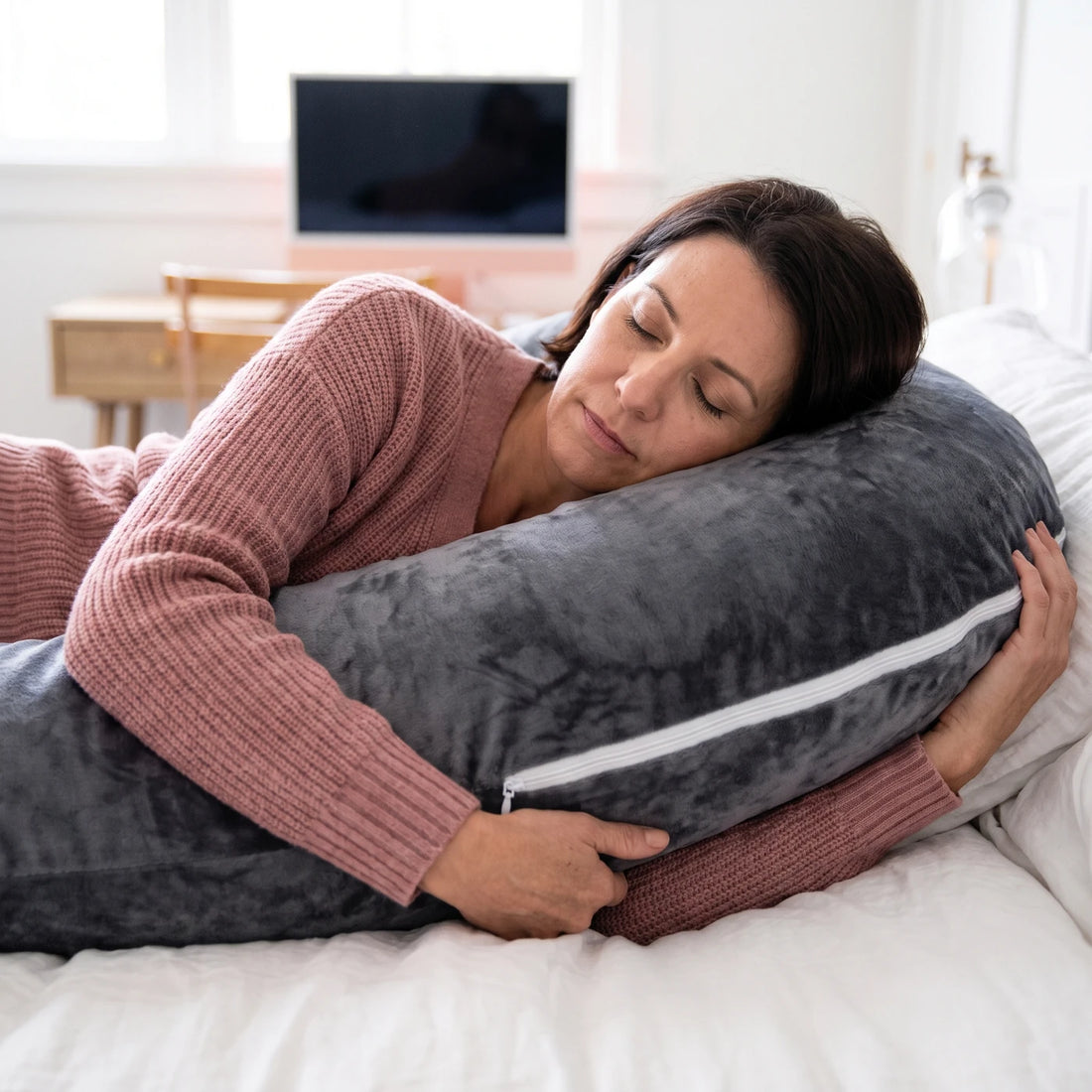 Une femme détendue, les yeux fermés, serre son coussin en U gris velours
