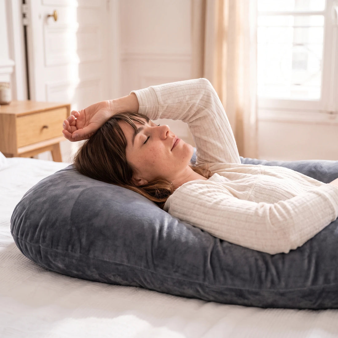 Une femme allongée, la main sur le front, totalement détendue contre son coussin en U