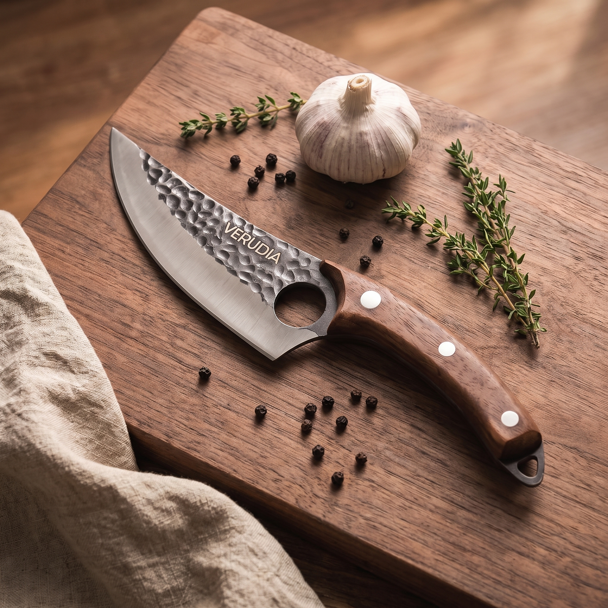 Couteau de chef Verudia posé sur une planche en noyer avec ail et thym